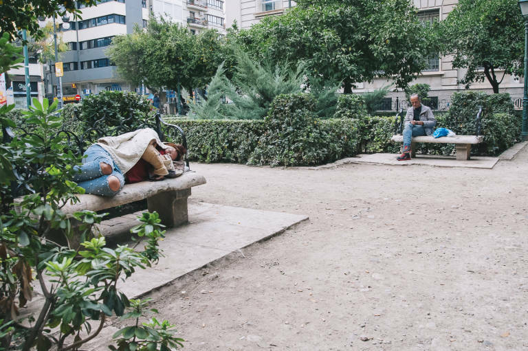 Una mendigo duerme mientras otro fuma un cigarro en un jardín de València. Foto: KIKE TABERNER