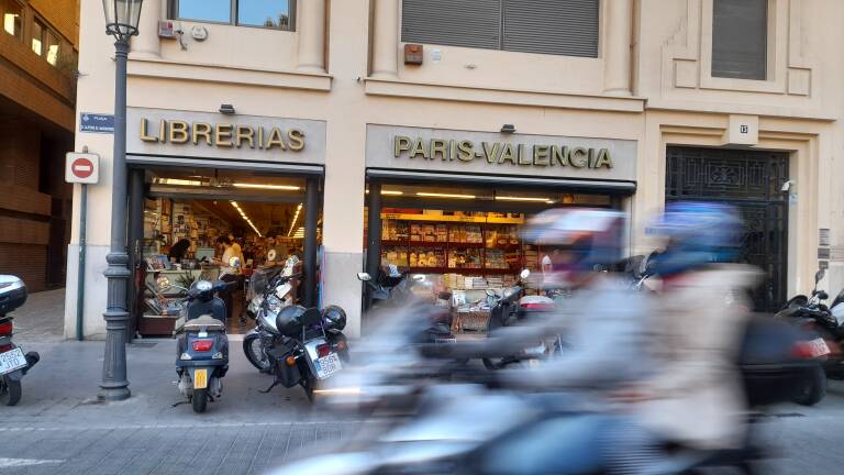 Unos motoristas pasan por delante de una librería de París-Valencia.